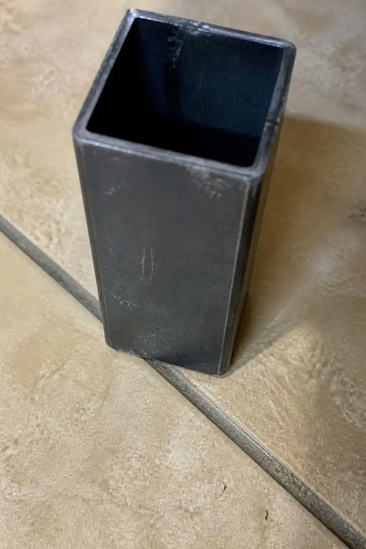 A square metal chair leg standing on a tiled floor with its open end uppermost