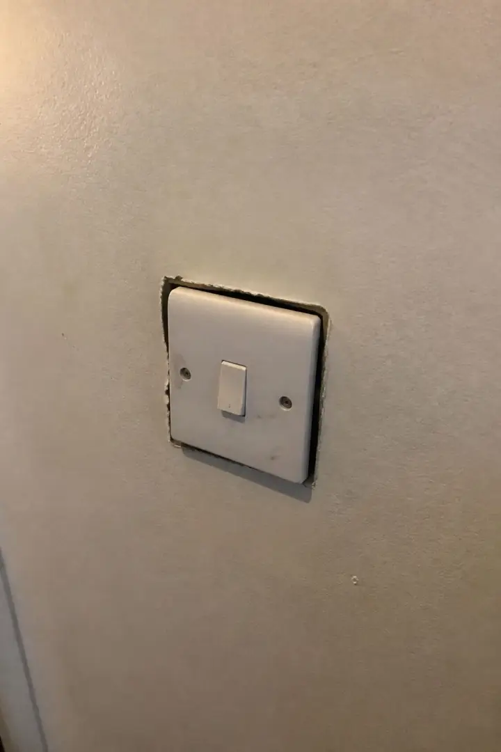 A white light switch on a cream wall, standing proud of the plaster with a dark gap round it
